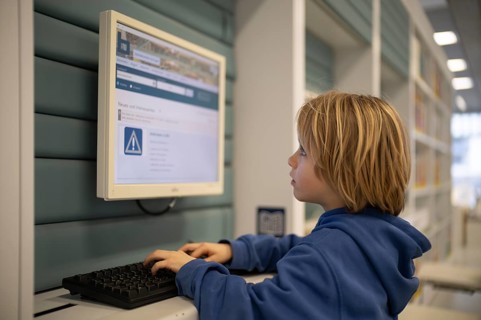 Interior shot, boy, 6 years old, blonde, operating computer, PC station, city library catalog,