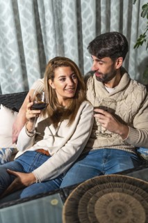 Happy couple enjoying a romantic evening, drinking wine on their sofa, creating a cozy and intimate