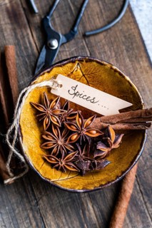 Top view of star anise and cinnamon sticks in a decorative yellow bowl, with a Spices written tag,