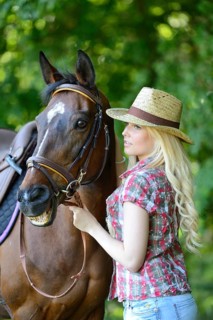 Woman (cowgirl) in a straw hat, plaid shirt and denim shorts stands beside a polish arabian horse