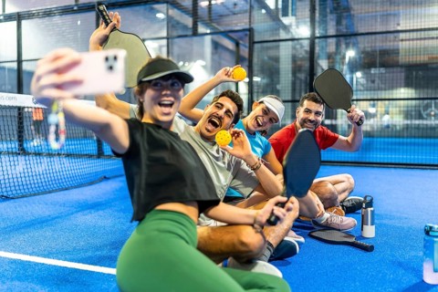 Group of enthusiastic friends capturing a joyful selfie moment on the pickleball court, holding