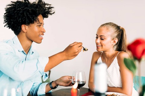 A couple enjoys a romantic dinner, sharing food and conversation over glasses of wine. The warm