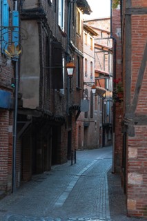 Narrow cobblestone alleyway bordered by brick buildings and aged wooden shutters, illuminated by