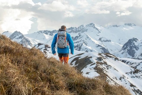 A man in outdoor gear treks along a scenic path in the Pyrenees mountains. Snow covered peaks