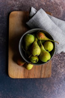 A top view of a bowl filled with fresh wild pears, resting on a wooden board. The rustic setting