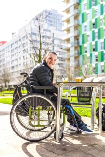 Young man in a wheelchair is smiling while having a drink with a friend at an outdoor table in the