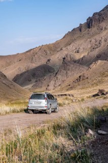 Off-road vehicle at the mountain pass at Songköl, gravel road at a plateau, mountains behind,