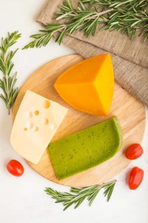 Green basil cheese and various types of cheese with rosemary and tomatoes on wooden board on a