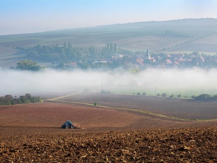 View of the village of Rhoden in autumn, fog sweeping through the valley, a tractor ploughs a