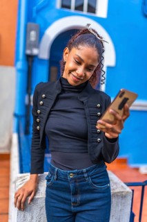 Beauty cool african american woman using smartphone leaning on a rail outside a blue vivid house