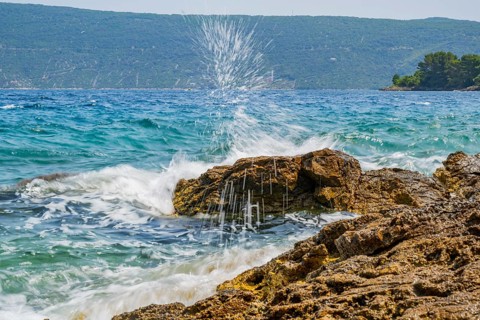 Wellen brechen an einem Felsen im Meer an einem sonnigen Tag auf der Insel Cres, Kroatien