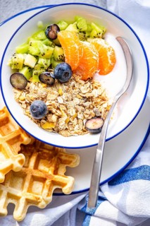 A vibrant breakfast bowl filled with kiwi, mandarin, and blueberries atop yogurt and granola,
