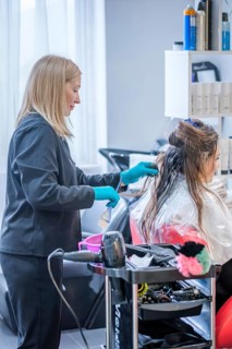 A woman receives a keratin hair treatment at a beauty salon. The hair stylist works carefully,