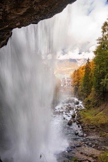 View through a waterfall onto an autumn landscape with mountains and a building, Lake Brienz,