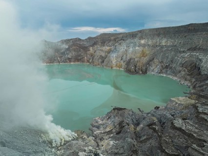A bright turquoise acidic lake lies inside Ijen volcano, with sulfur gas rising from vents on the
