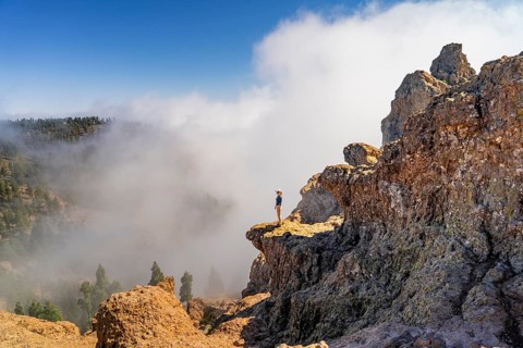 Distant unrecognizable person captured standing on a rugged cliff overlooking a misty landscape at