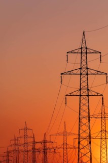 Silhouette of several high-voltage power lines and electricity pylons against a glowing orange and