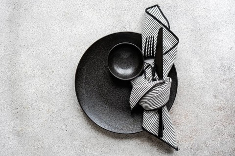 A minimalist black and white table setting features a textured black plate, a striped napkin, and