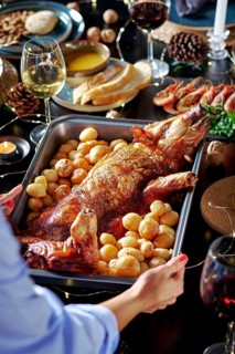 Cropped unrecognizable woman's hands serving in a sumptuously set dining table featuring a roasted