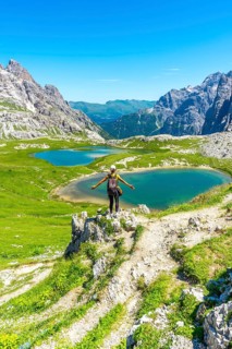 Female hiker with open arms savoring the stunning view of tre cime di lavaredo and alpine lakes in