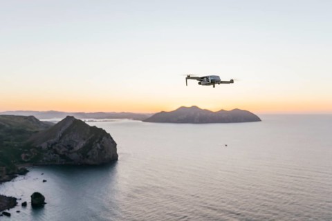 A drone gracefully flies over a tranquil coastal scene at sunset The tranquil ocean and silhouettes