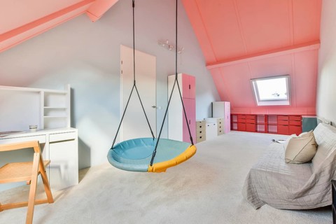 Attic room with a vibrant coral ceiling and soft carpet flooring. Features a white desk and chair