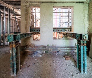 Interior view of a building under renovation. Visible scaffolding and steel beams support walls in