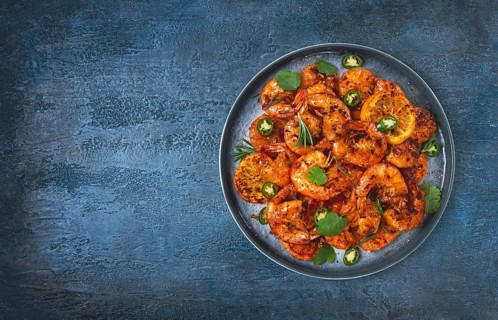 Grilled shrimp, unpeeled, headless, with spices, on a dark blue table, homemade, no people