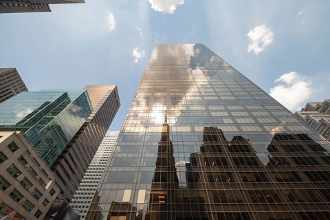 Upward view of a modern glass building in Manhattan, showcasing a reflection of the surrounding
