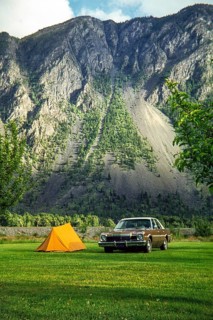 Dodge Aspen car parked in campsite by small two-man tent with mountain in background, unspecified