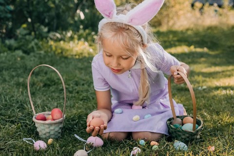 A young girl wearing bunny ears excitedly searches for colorful eggs during an Easter egg hunt,