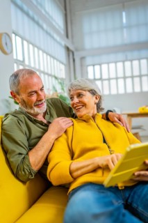 Vertical photo of a modern senior couple relaxed at home using digital tablet together