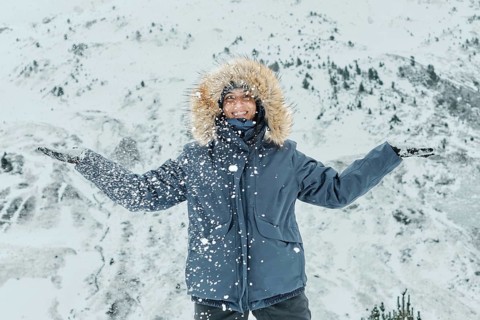 A woman, bundled in a fur-lined jacket, joyfully embraces the snowfall at Astun ski resort, nestled