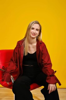 A young woman with blonde hair sits comfortably on a sleek red chair against a vivid yellow