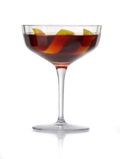 Cocktail in a coupette glass against a white background, a wide lemon zest as garnish, studio shot