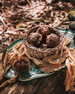 A woven basket filled with freshly baked pumpkin muffins rests on a decorative tray. The autumn