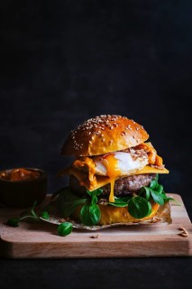 A delectable gourmet burger topped with melted cheese, egg, and greens, captured on a rustic wooden