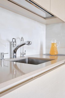 A bright and modern kitchen displays a stainless steel faucet and a clean sink. A pitcher of orange