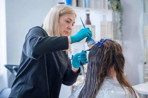 In a beauty salon, a hair stylist works on a woman's hair, applying keratin treatment for hair