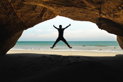 A man jumps inside a cave at Mancora Beach, Peru, creating a striking silhouette against the ocean