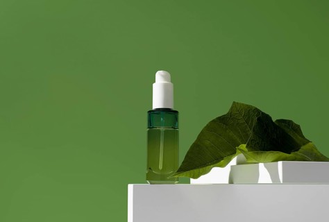 A sleek bottle of essential oil presented on a white stand, highlighted by a fresh green leaf on a