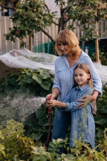 A mother and daughter enjoy a sunny day gardening together. They water plants in their small