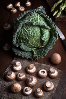 A fresh cabbage sits alongside mushrooms on a rustic wooden table, creating a natural and earthy