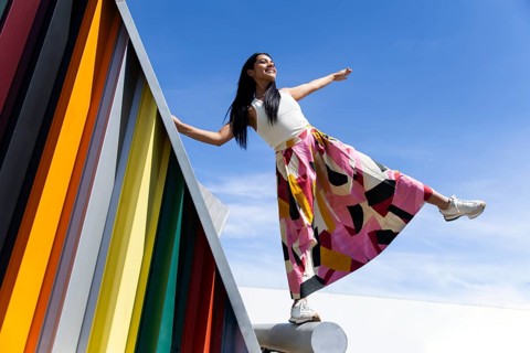 A woman in a colorful outfit poses vibrantly against a backdrop of modern architecture, creating a