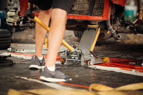 A mechanic works on a racing car in a garage, using a hydraulic jack for adjustments. The scene