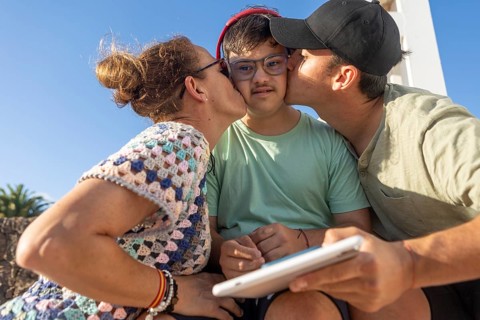 Mother and brother share a sweet moment kissing their Down Syndrome teenager outdoors, creating a