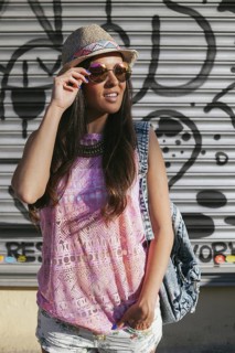 Stylish woman wearing a straw hat and sunglasses stands confidently in front of urban graffiti.