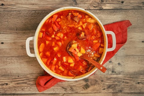A large pot on a wooden table filled with a stew made of meat, potatoes, carrots, and other