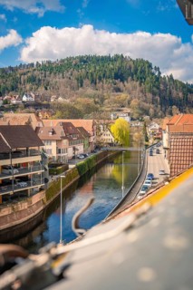 River bank with view of houses and wooded hills in the background, Calw, Black Forest, Germany