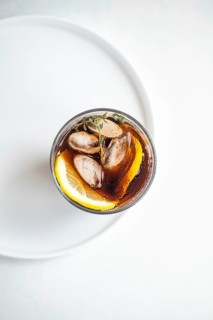 A refreshing gin cocktail with cola drink garnished with fresh thyme and a lemon slice, served over